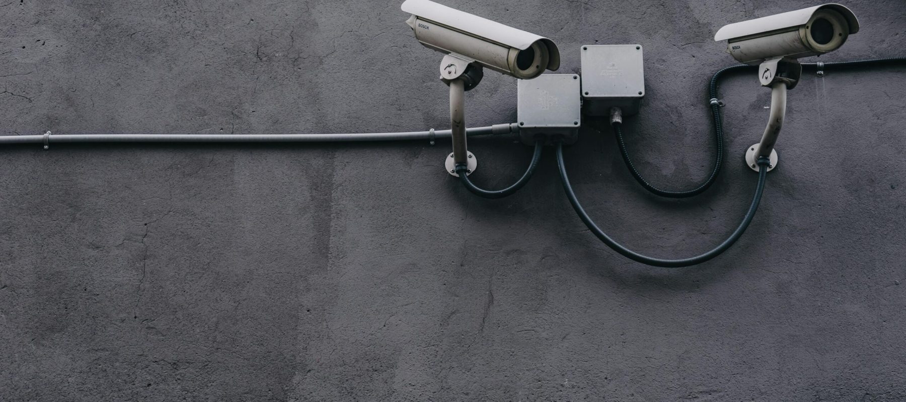 Two surveillance cameras mounted on a concrete wall, highlighting security technology.